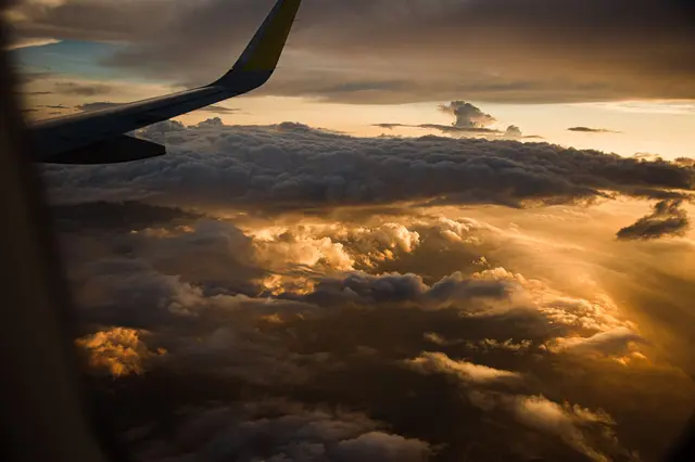 Aeroplane wing above golden clouds at sunset